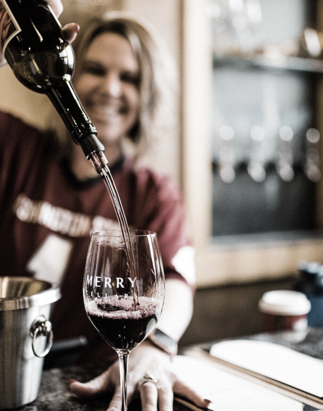 A person pouring wine into a glass that reads Merry Cellars.